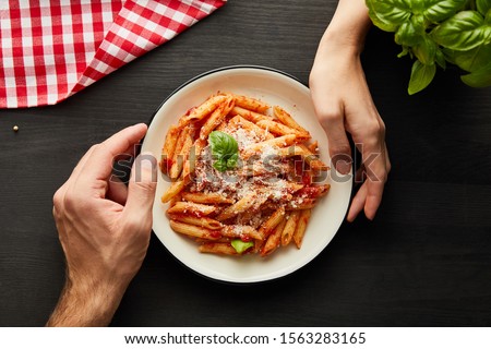 cropped view of couple holding plate with tasty bolognese pasta on black wooden table with basil, cutlery and check napkin Royalty-Free Stock Photo #1563283165