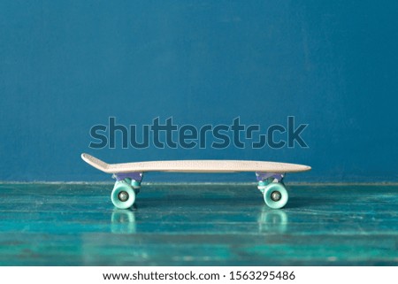Plastic skateboard on the green wooden floor against blue wall. Side view