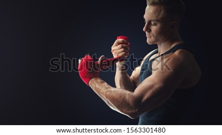 Man is wrapping hands with red boxing wraps isolated on black background Strong hands and fist, ready for training and active exercise Shot at studio on black background