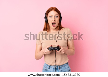 Young redhead woman over isolated pink background playing at videogames
