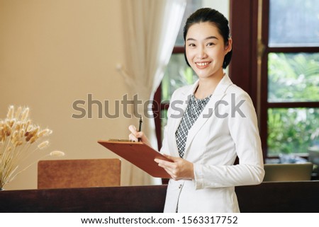 Portrait of lovely spa salon manager taking notes in document on clipboard in her hands