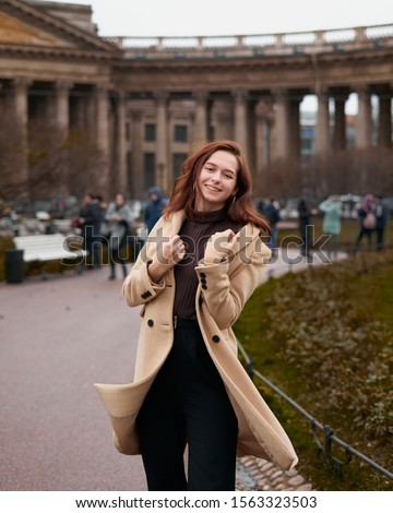 Beautiful funny naughty stylish fashionable happy girl dancing on streets of St. Petersburg city. Charming smiling woman with long dark hair, vertical. Autumn, winter