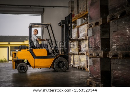 Warehouse man worker with forklift. Warehouse worker driver in loading by forklift stack loader Royalty-Free Stock Photo #1563329344