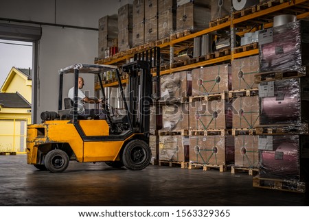 Warehouse man worker with forklift. Warehouse worker driver in loading by forklift stack loader Royalty-Free Stock Photo #1563329365
