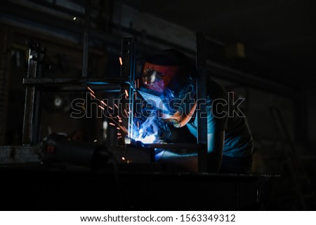 A man in a helmet works with a welding machine and sparks fly in all directions