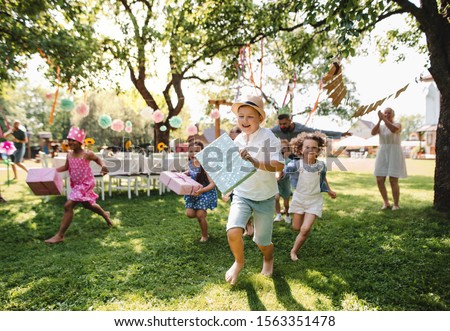 Small children ruunning with present outdoors in garden on birthday party.