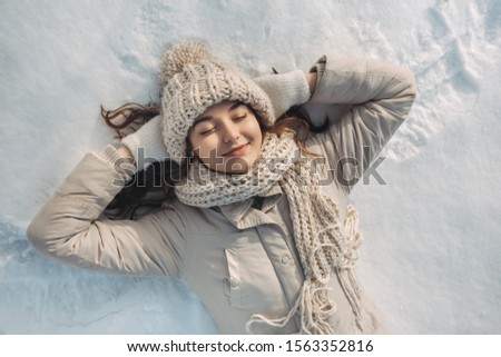 Portrait of a beautiful young woman laying down with closed eyes on a frozen snow lake playing games during a sunny winter vacation. Mixed race Asian Caucasian gorgeous girl resting during winter