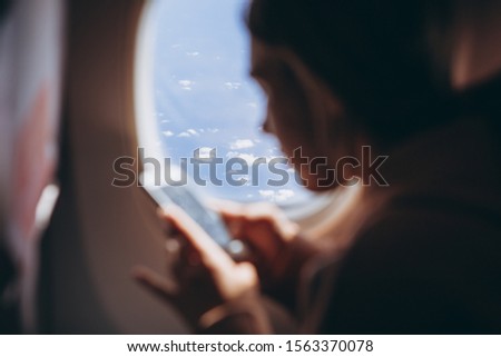 selective focus, noise effect: girl who flies for the first time and sits on a chair by the window enjoys the view from the window, takes pictures, is happy about her first flight on the plane, 