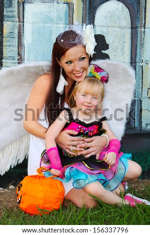 Mother dressed as an angel and a little girl dressed as a rock star pose for a picture