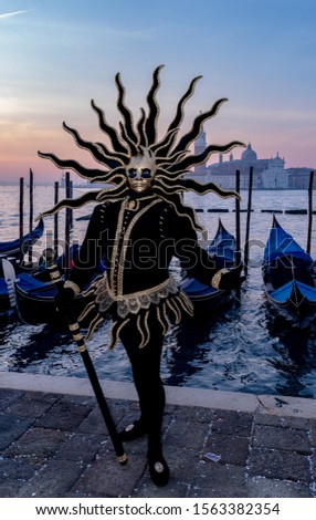 A vertical shot of a male wearing a black costume and an exotic mask standing by the sea