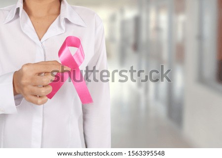 Close-up Woman holding pink ribbon in hospital blur background. Breast cancer awareness or Ribbon Formed Aids Symbol concept.