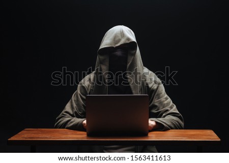 Hacker without a face in a hood with a laptop on a black background