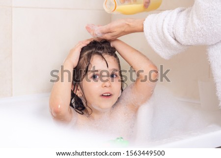 Mother washed kid hair with shampoo in the bathroom. Portrait of a beautiful brunette little girl with wet hair, blue eyes, 6 years old.