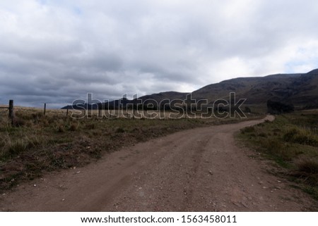 Dirt road in mountains area with cloudy sky.