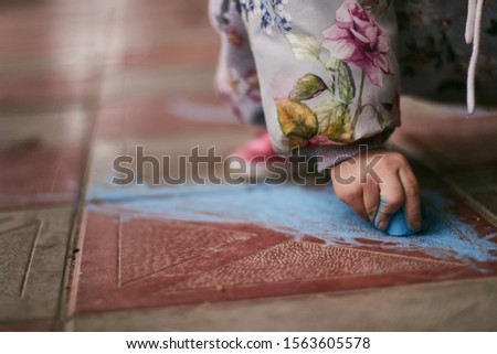 Kid drawing with a blue chalk on the ground