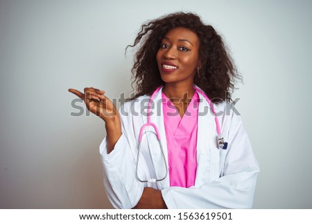 African american doctor woman wearing  pink stethoscope over isolated white background with a big smile on face, pointing with hand and finger to the side looking at the camera.
