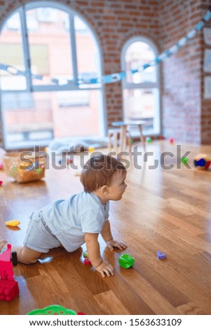 Adorable toddler sitting on the floor playing with toys at kindergarten