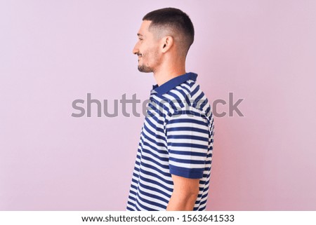 Young handsome man wearing nautical striped t-shirt over pink isolated background looking to side, relax profile pose with natural face with confident smile.