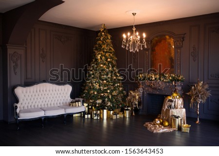 Interior of luxury modern living room with fireplace, comfortable sofa and chandelier decorated with golden Christmas tree and gifts