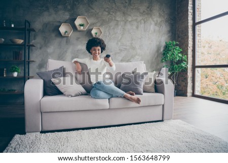 Photo of pretty dark skin wavy lady homey mood holding tv remote control changing channel searching favorite humor show sitting cozy couch casual outfit flat indoors