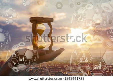 The concept of global business. Hand holding hourglass on the background of the city and business icons.