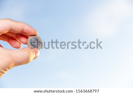hand holding 1 euro coin over clear blue sky, Exchange money. Financial concepts, Business Concept.