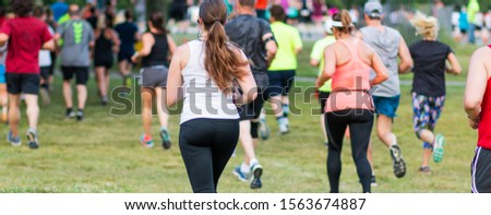 Rear view of many runners racing a 10K on grass at Sunken Meadow State Park in New York. Royalty-Free Stock Photo #1563674887