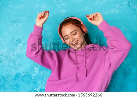 Photo of delighted attractive woman in headphones listening music and dancing isolated over blue wall indoors