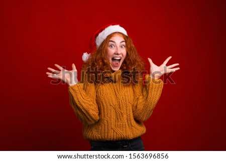 Photo of surprised young woman standing over red background and wearing santa claus hat