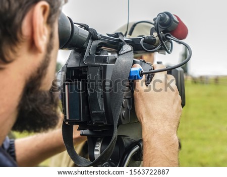 video camera, cameramanon green grass field background.photographer records the sunset in the background of meadow.Professional videographer on adventure vacation shooting camera on steadicam.
