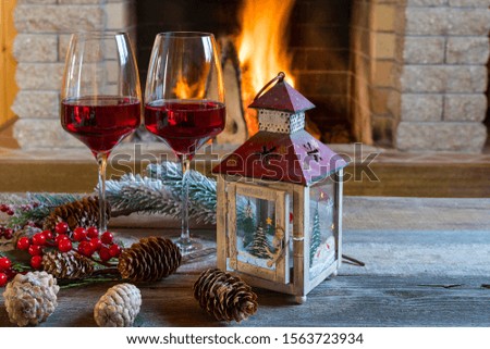 Christmas, New year. Two glasses of red wine, christmas lantern and decorations near cozy fireplace, in country house, winter vacation.