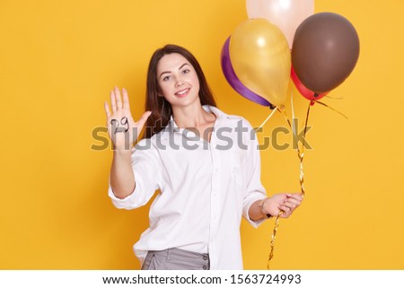 Image of cheerful beautiful young woman standing and showing inscription twentie nine on her palm isoalted over white background, modelposing with multi colored balloons. Holidy celebration concept.