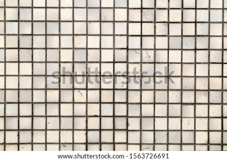 Wall / floor made of small light yellow / beige square tiles. Surface of an exterior wall of a building. Beautiful clean, symmetric architectural details of a building. Color image.