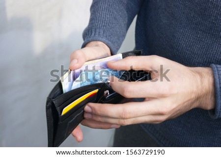 A young man counts his money in a black leather wallet. Hryvnia is the official national currency of Ukraine. National Bank of Ukraine