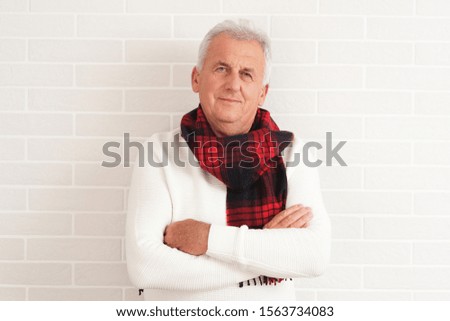 Older grey man in white sweater and red scarf.