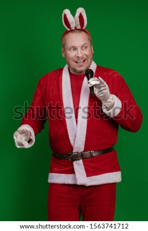 Emotional male actor in a costume of Santa Claus sings and speaks into a microphone and poses on a green chrome background