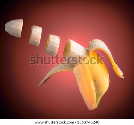 Sliced flying ripe banana isolated on coral pink gradient with black background. Floating dark food photography with copy space.