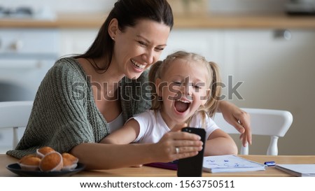 Head shot smiling young mother showing funny cartoons to overjoyed little adorable girl on smartphone. Happy 30s woman recording family video with laughing small preschool daughter on mobile phone.