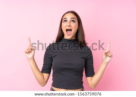 Young girl over isolated pink background surprised and pointing up