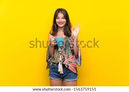 Caucasian girl in colorful dress over isolated yellow background holding hot cup of coffee