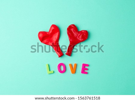 two red rubber balloons blow away in the shape of a heart on a green background