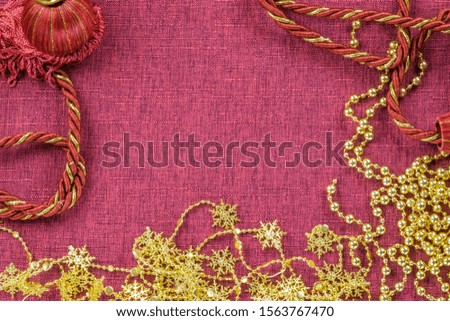 Background in the form of a chain of golden snowflakes, beads and a braided rope brush for Christmas decorations on a burgundy background, top view
