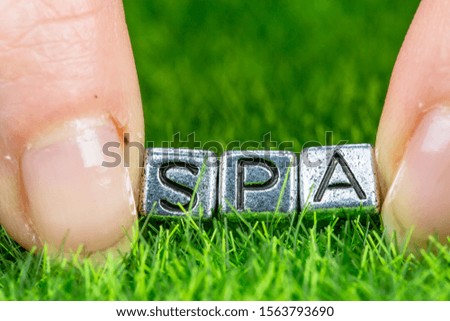 Close up on word SPA written in metal letters laid on grass and held between the fingers of a woman. Concept of wellness background
