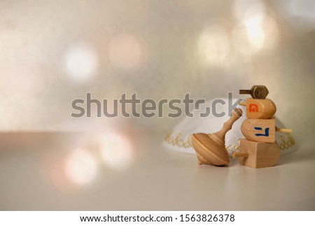 concept of of jewish religion holiday hanukkah with wooden and brass spinning top toys (dreidels), and traditional skullcap (yarmulka, kipa) over wooden table and bright background