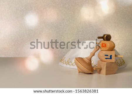 concept of of jewish religion holiday hanukkah with wooden spinning top toys (dreidels), and traditional skullcap (yarmulka, kipa) over wooden table and bright background
