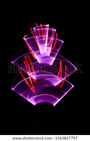Curved abstract shapes made of red light saber in background. Lightpainting session in long exposure at night. 