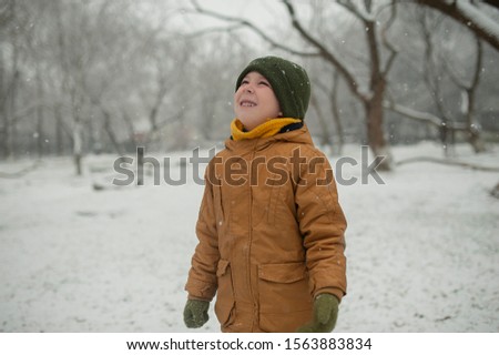 
cheerful kid in a yellow down jacket and military hat rejoices at snow in winter catches snowflakes on his face