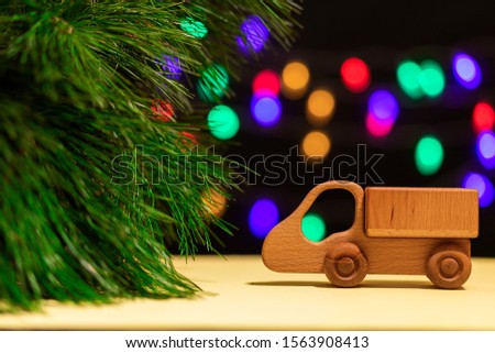Сlose-up a wooden truck drove up to a Christmas tree against the background of many colorful lights. Picture for New Year's design, greeting card.