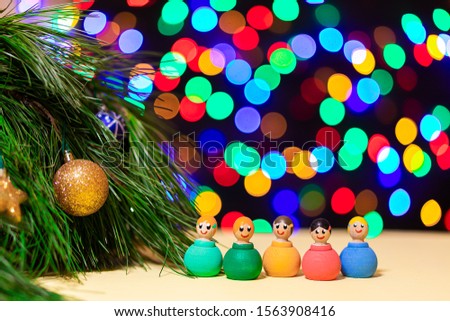 close-up wooden multi-colored little men lead a round dance and enjoy the holiday near the New Year tree against the background of many colorful lights. Picture for New Year's design, greeting card.