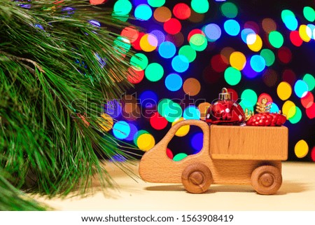 a close-up of a wooden truck brought red Christmas balls to a Christmas tree on the background of many colorful lights. Picture for New Year's design, greeting card.